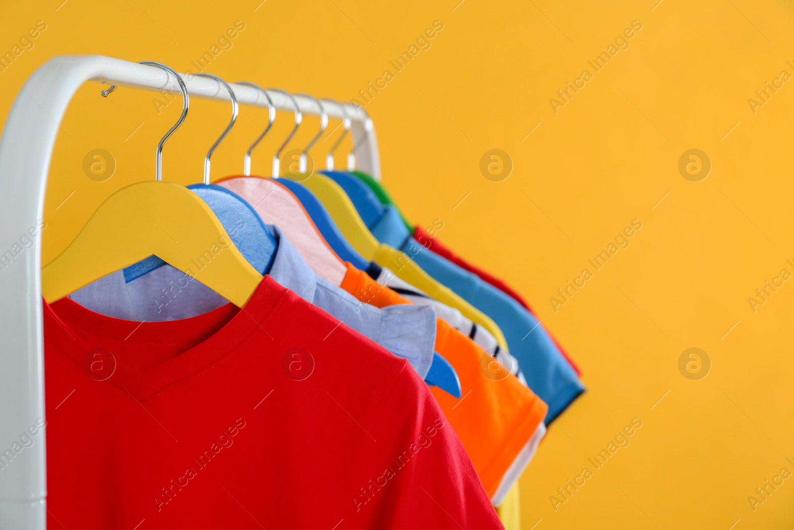 Photo of Rack with stylish children clothes on yellow background, closeup. Space for text