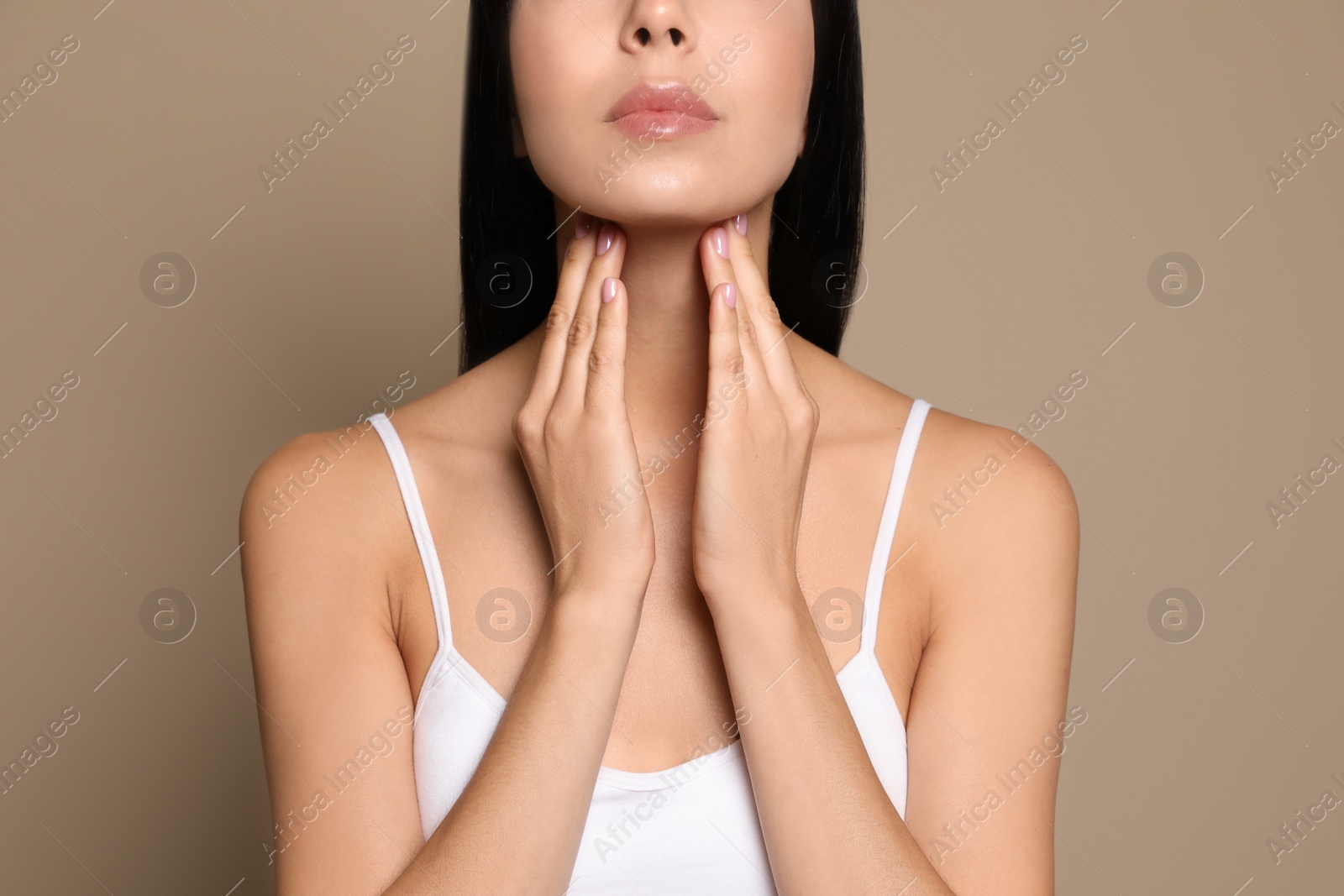 Photo of Young woman doing thyroid self examination on beige background, closeup