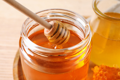 Dripping tasty honey from dipper into glass on table, closeup