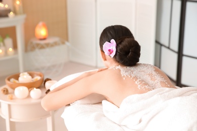 Photo of Beautiful young woman with body scrub on her back in spa salon