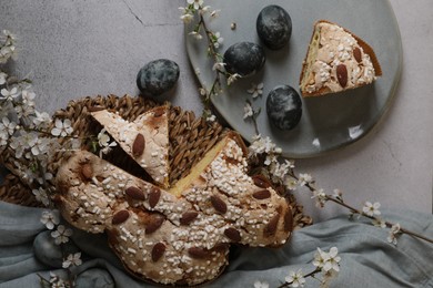 Photo of Delicious cut Italian Easter dove cake (traditional Colomba di Pasqua), painted eggs and flowering branches on grey textured table, flat lay