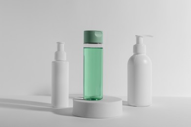 Photo of Bottles with different cosmetic products and podium on white background
