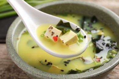 Photo of Delicious miso soup with tofu in spoon above bowl, closeup