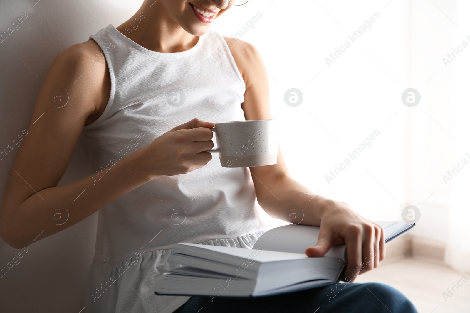 Photo of Young woman with cup of coffee reading book on light background, closeup