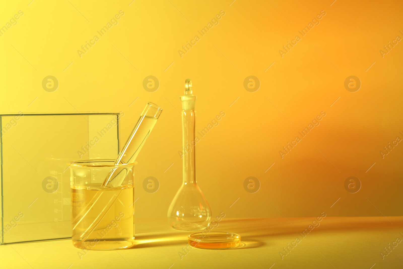 Photo of Laboratory analysis. Different glassware on table against yellow background, space for text