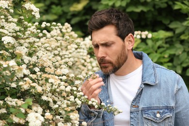 Man suffering from seasonal pollen allergy near blossoming tree on spring day