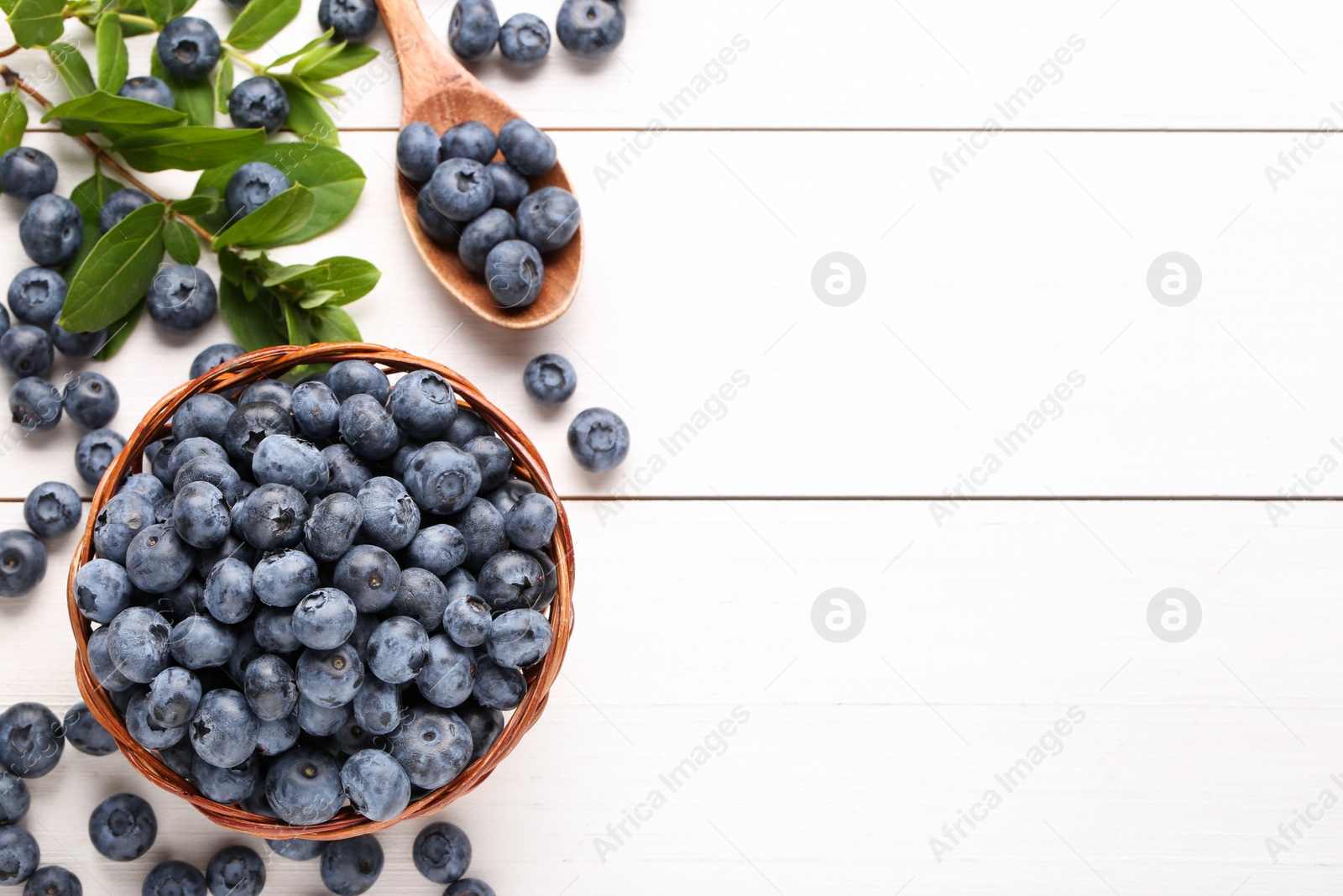 Photo of Tasty fresh blueberries and green leaves on white wooden table, flat lay. Space for text