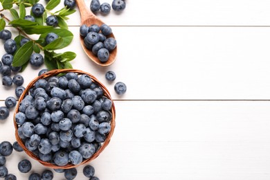 Photo of Tasty fresh blueberries and green leaves on white wooden table, flat lay. Space for text