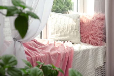 Photo of Soft pillows and plaids on sunlit window sill in room. Cozy place to relax