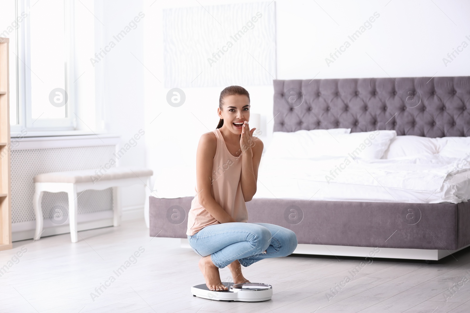 Photo of Surprised young woman measuring her weight using scales at home. Weight loss motivation