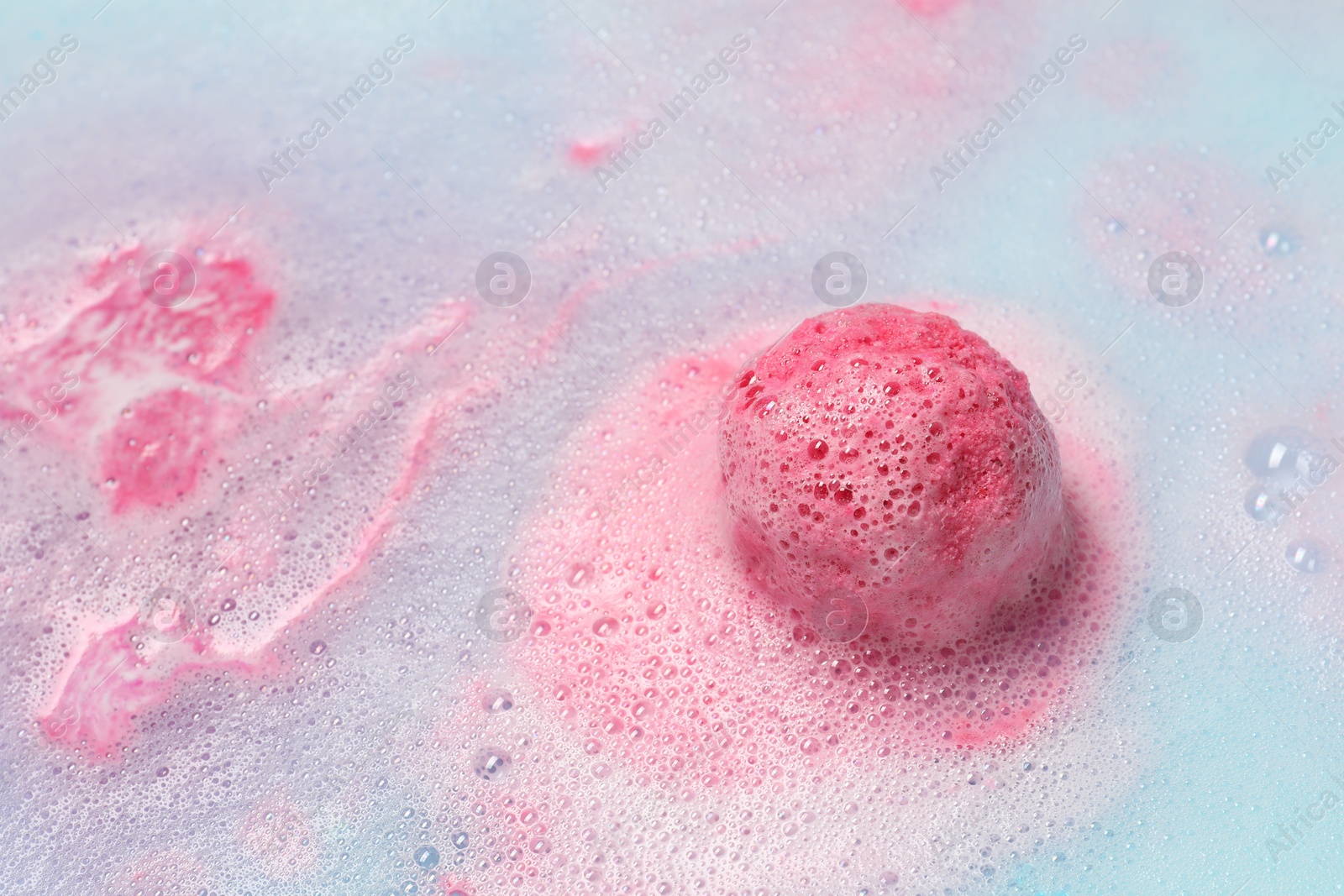 Photo of Pink bath bomb dissolving in water. Space for text