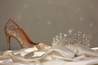 Beautiful silver tiara with diamonds near shoe on white cloth