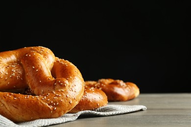 Tasty freshly baked pretzels on wooden table against black background. Space for text