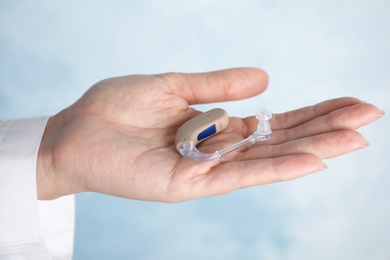 Doctor holding hearing aid on color background, closeup. Medical device