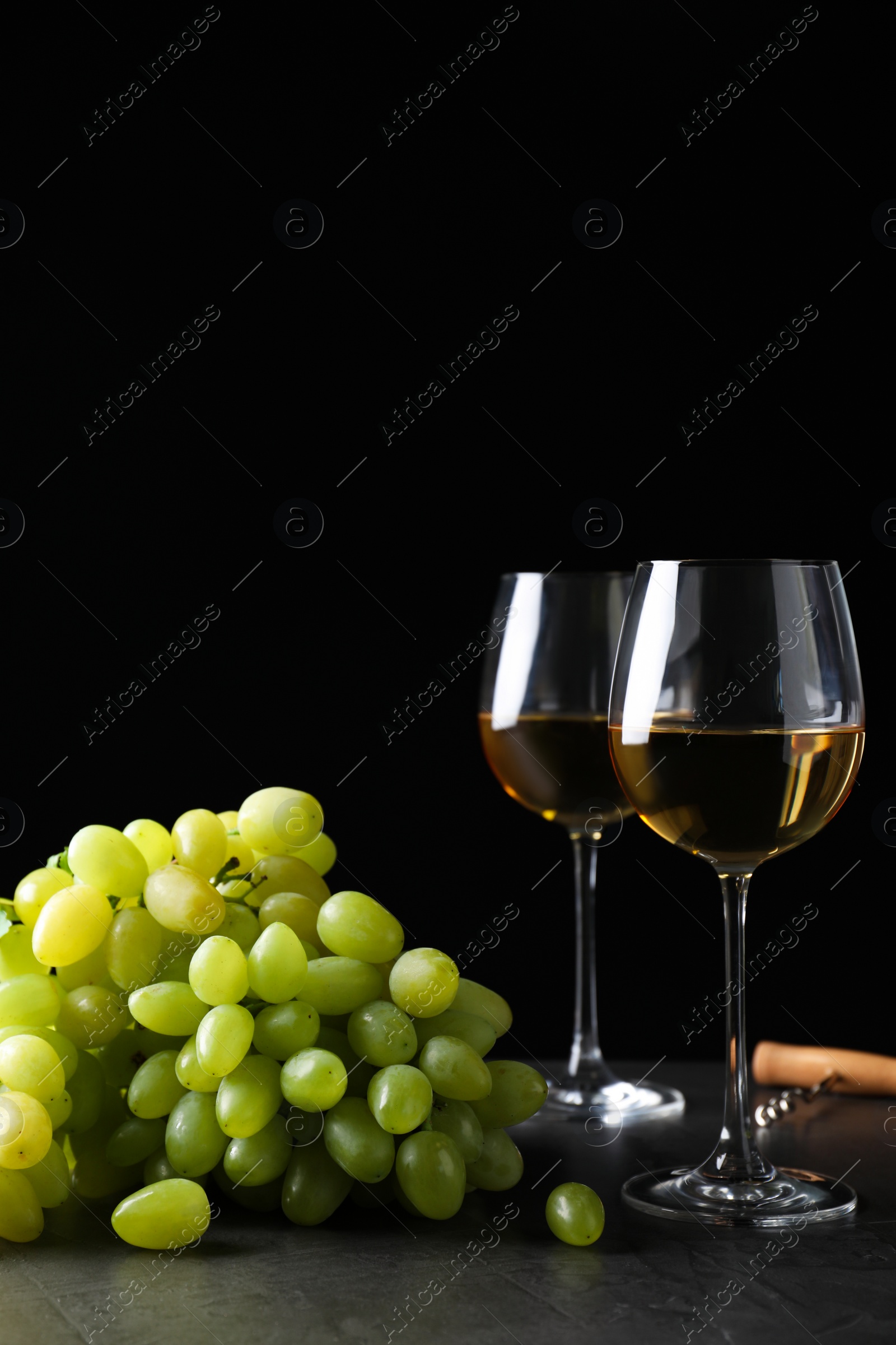 Photo of Fresh ripe juicy grapes with wineglasses on grey table against black background, space for text