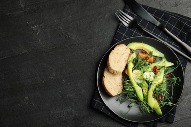 Photo of Salad with fresh organic microgreen in plate on black table, top view. Space for text