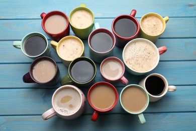 Many cups of different coffee drinks on light blue wooden table, above view