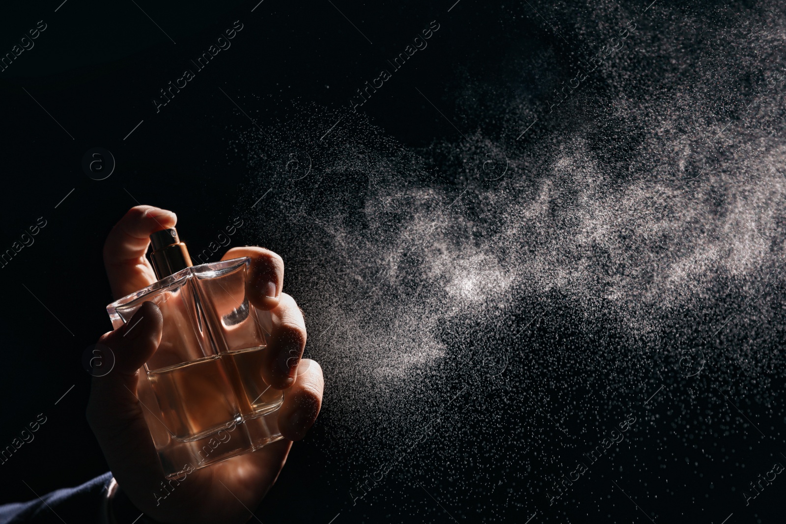 Photo of Man spraying luxury perfume on black background, closeup