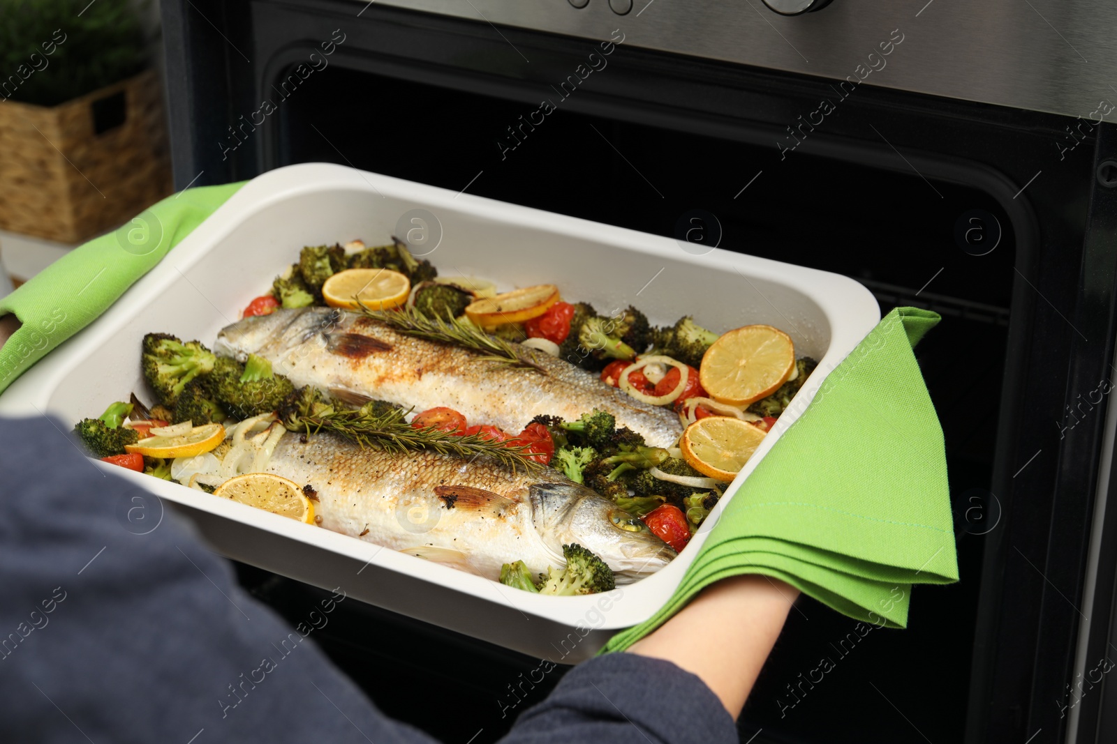 Photo of Woman taking baking dish with delicious fish and vegetables from oven, closeup