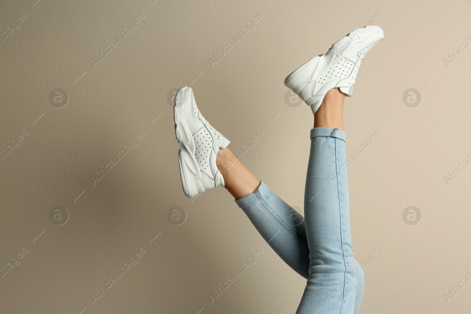 Photo of Woman wearing sneakers on beige background, closeup