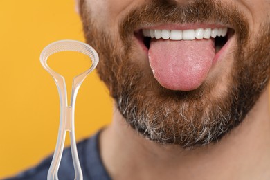 Photo of Man with tongue cleaner on yellow background, closeup