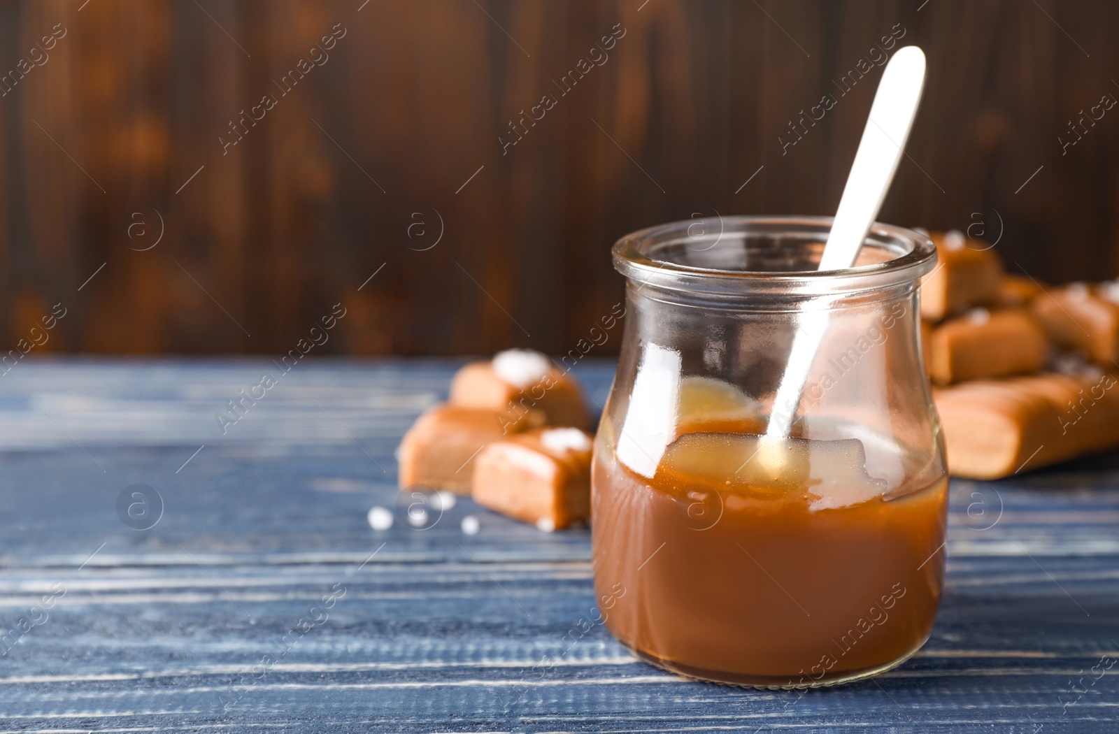 Photo of Salted caramel in jar on blue wooden table. Space for text