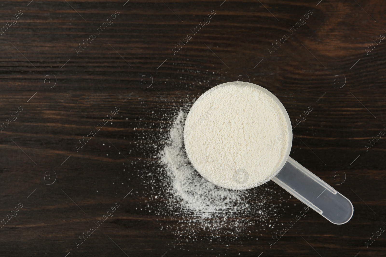 Photo of Measuring scoop of protein powder on wooden table, top view. Space for text