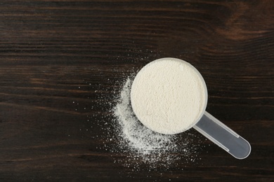 Measuring scoop of protein powder on wooden table, top view. Space for text