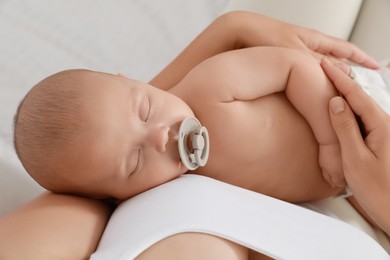 Mother holding her cute sleeping baby with pacifier at home, top view