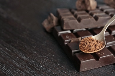 Spoon with cocoa powder and tasty chocolate on dark table, closeup