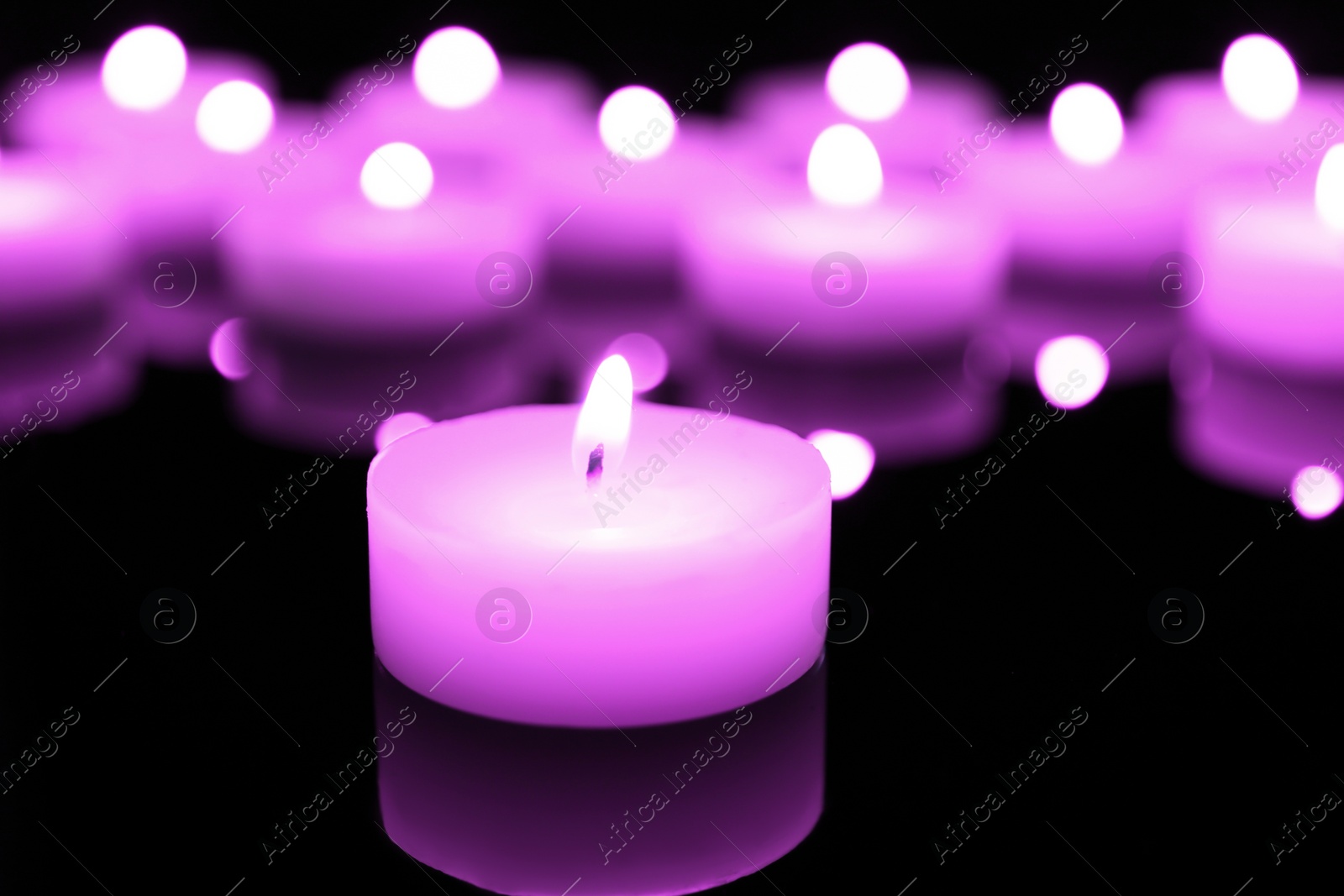 Image of Burning violet candle on black background, closeup. Funeral attributes