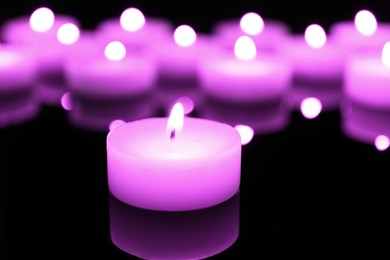 Burning violet candle on black background, closeup. Funeral attributes