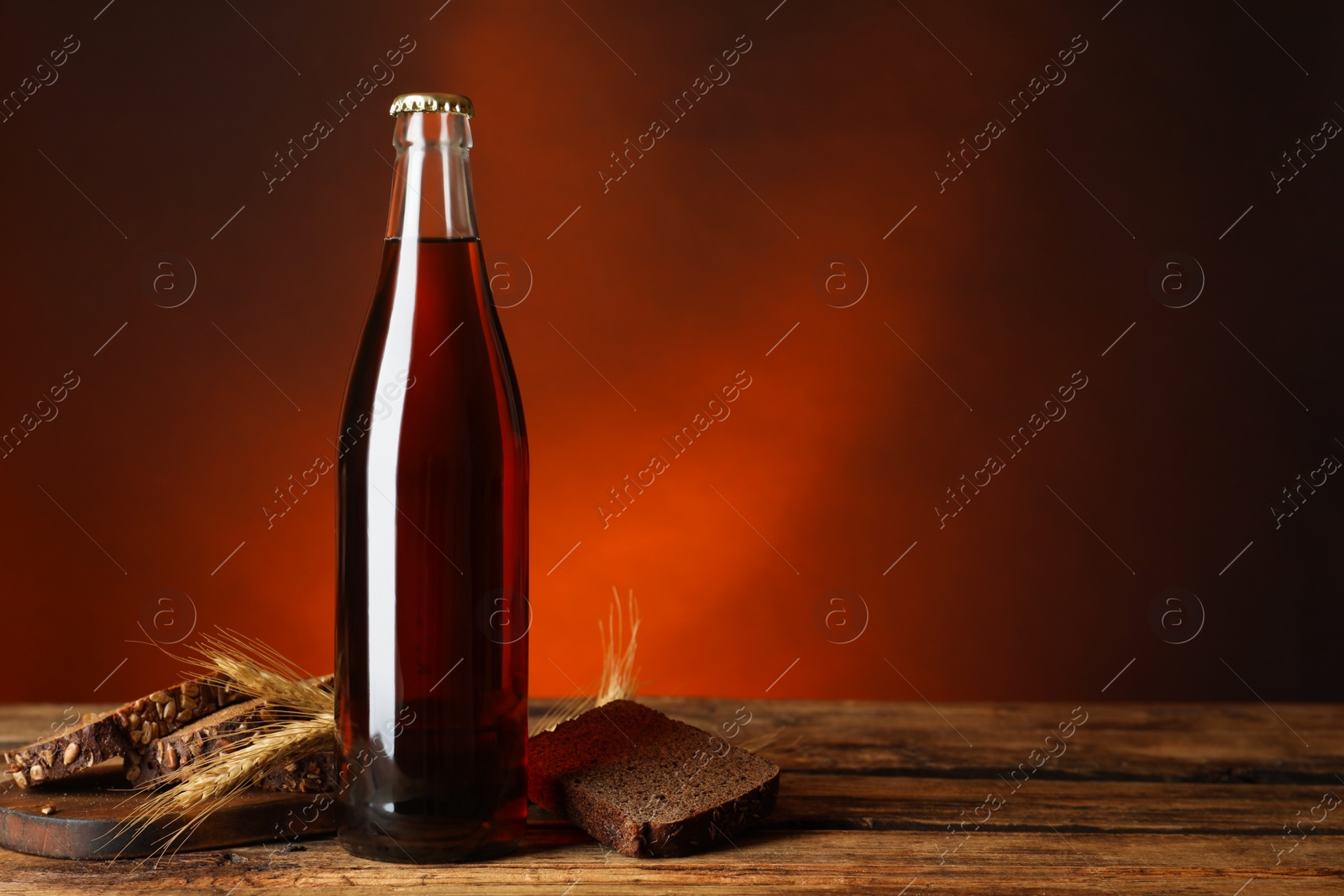 Photo of Bottle of delicious fresh kvass, spikelets and bread on wooden table. Space for text