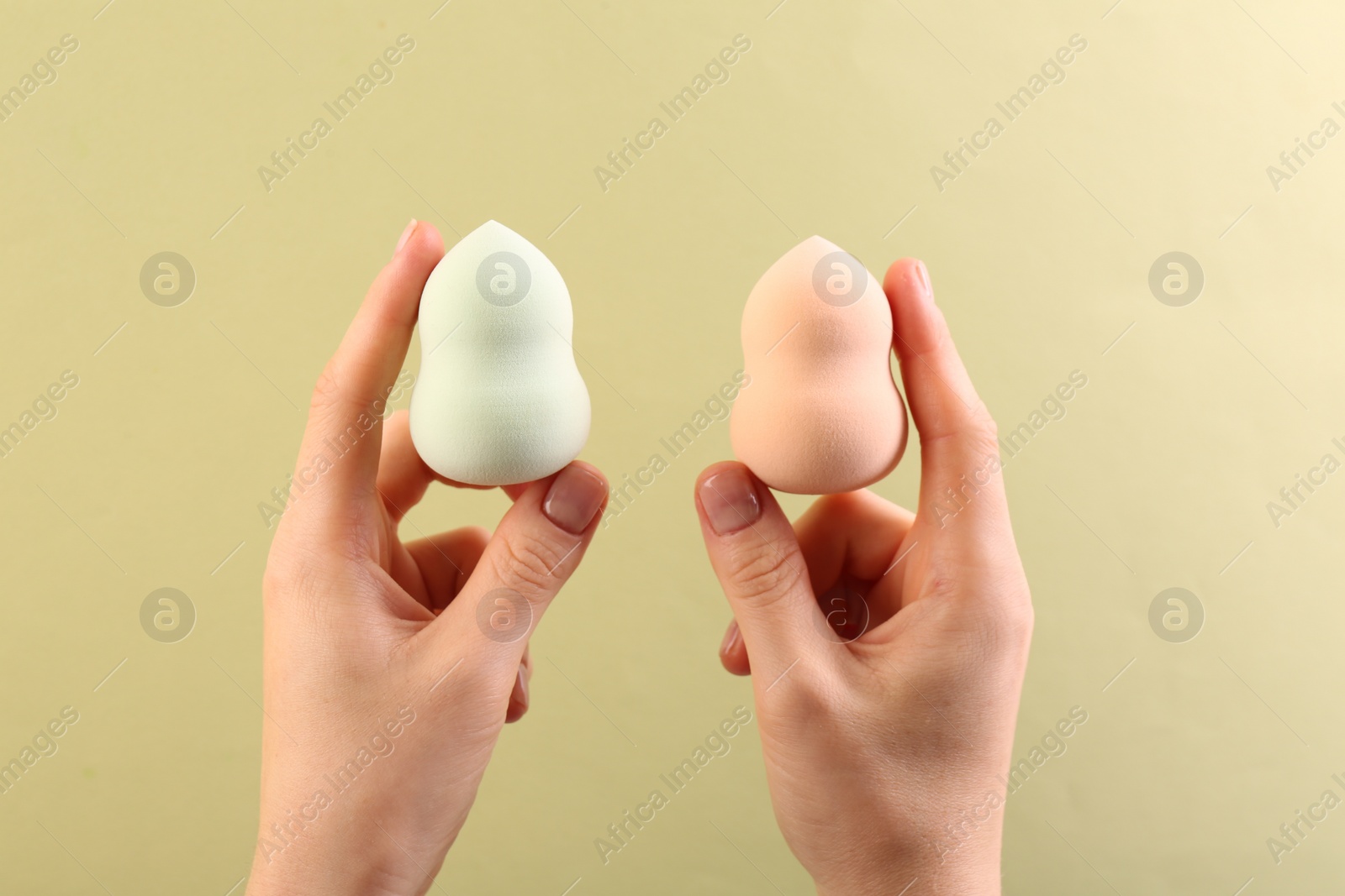 Photo of Woman with makeup sponges on light yellow background, closeup