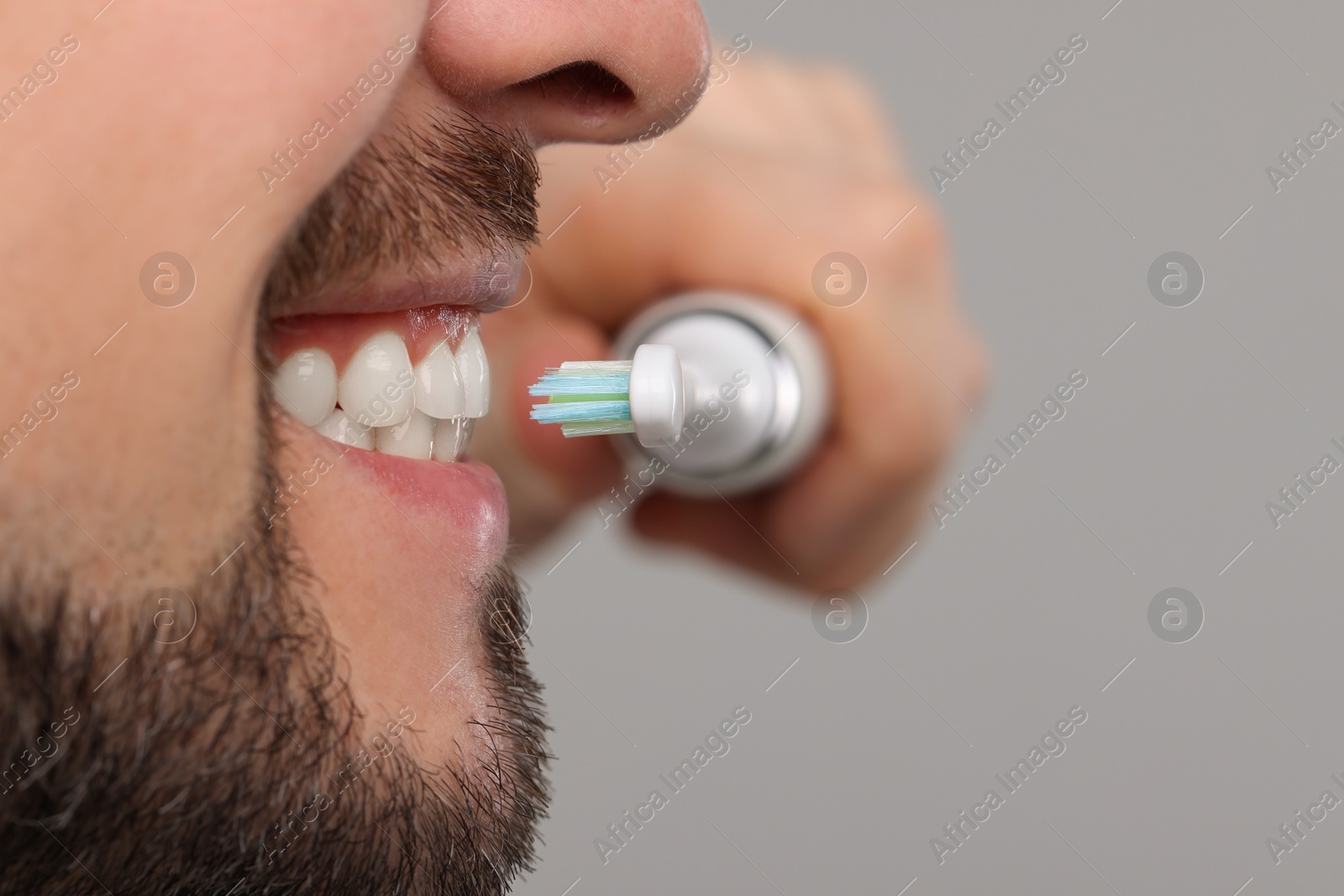 Photo of Man brushing his teeth with electric toothbrush on light grey background, closeup. Space for text