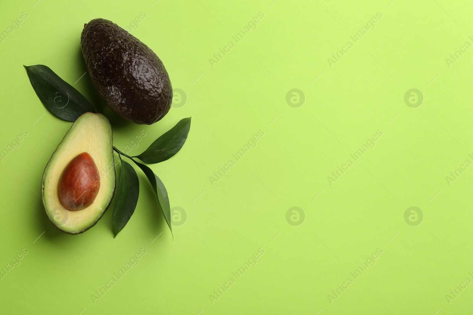 Photo of Ripe avocadoes and leaves on green background, flat lay. Space for text