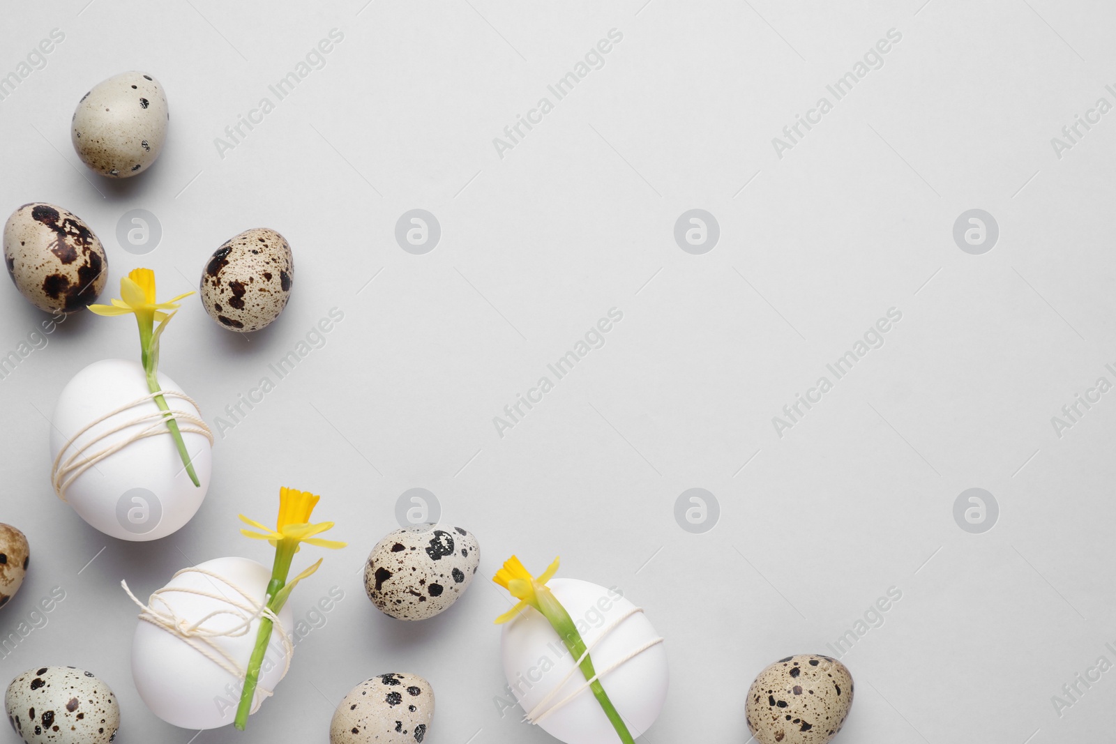 Photo of Easter eggs decorated with flowers on light grey background, flat lay. Space for text