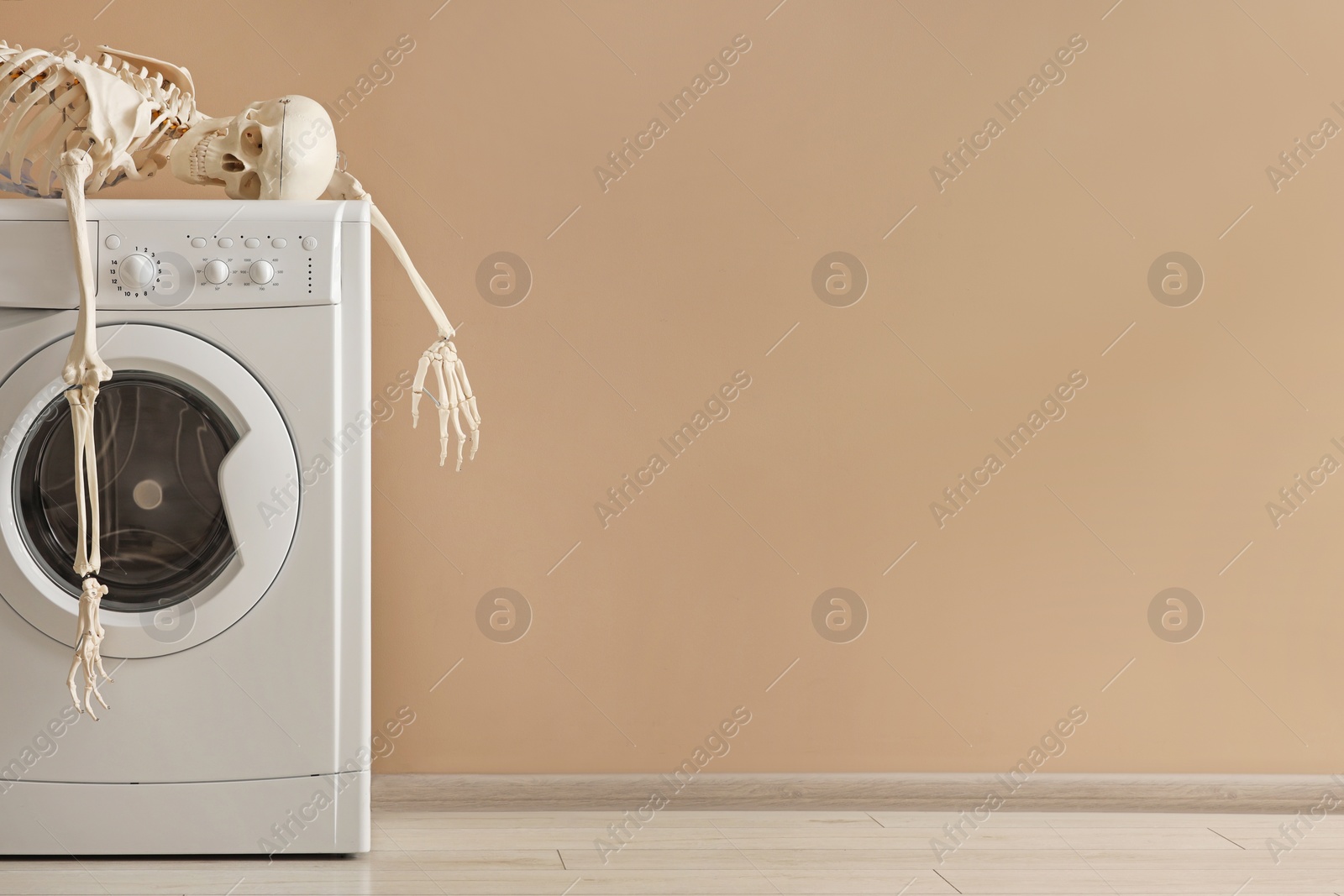 Photo of Waiting concept. Human skeleton lying on washing machine near beige wall indoors, space for text