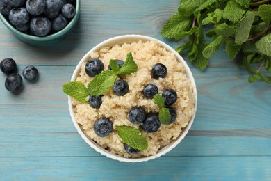 Tasty quinoa porridge with blueberries and mint in bowl on light blue wooden table, flat lay