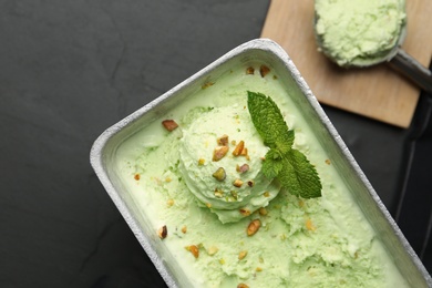Photo of Container of sweet pistachio ice cream on black table, top view
