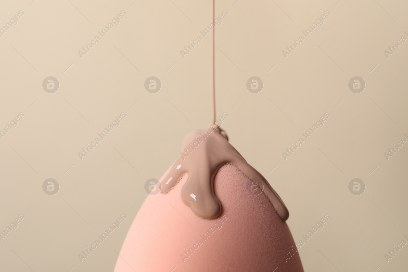 Photo of Skin foundation pouring onto makeup sponge on beige background