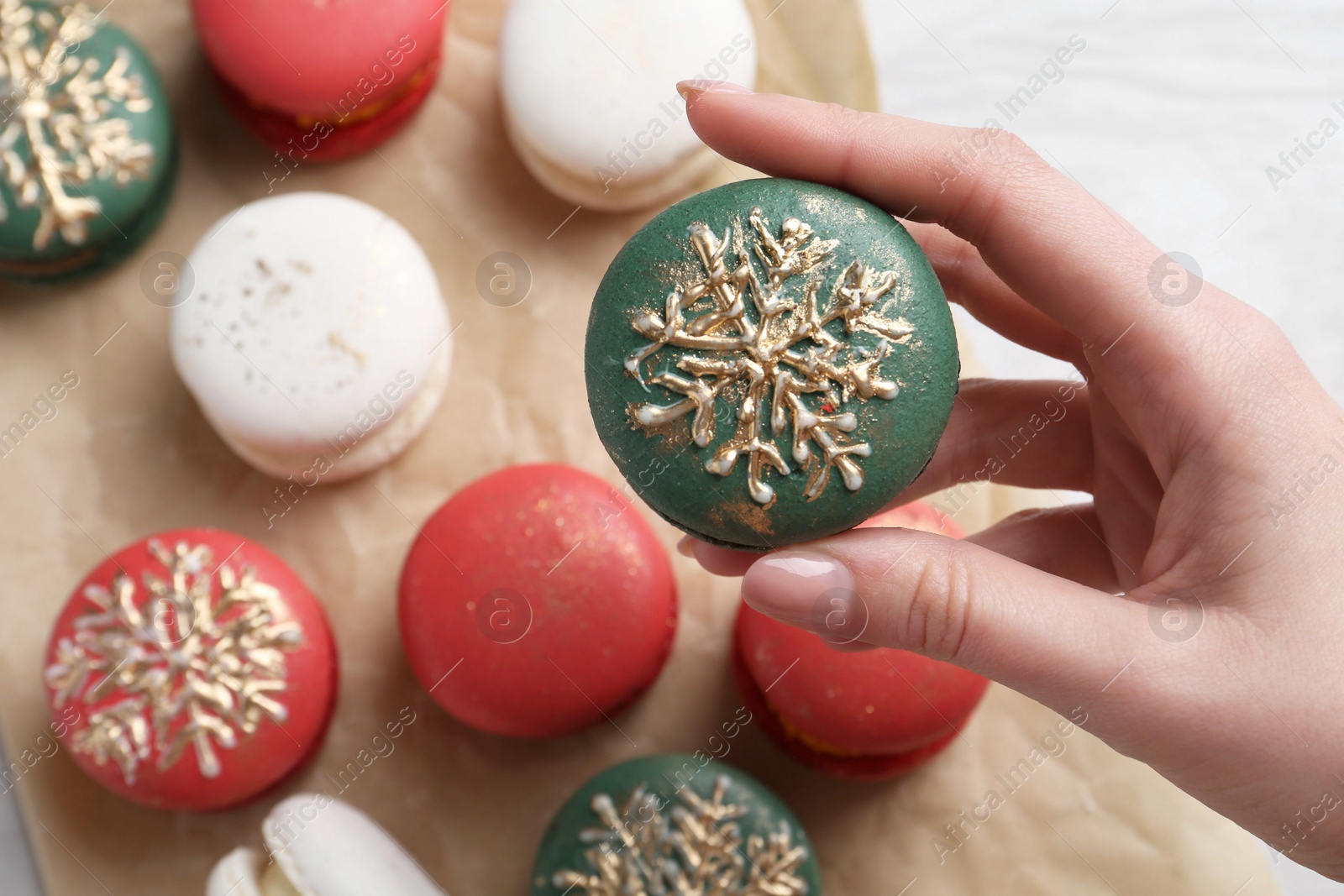 Photo of Woman with decorated Christmas macaron at table, closeup