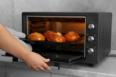 Photo of Woman taking out baking pan with delicious spiral buns from electric oven, closeup