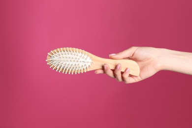 Photo of Woman holding wooden hair brush against crimson background, closeup