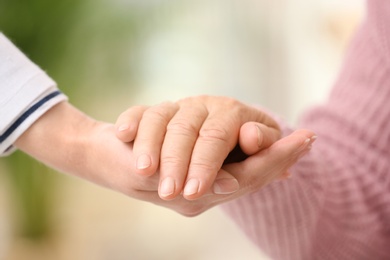 Photo of Nurse holding hand of elderly woman against blurred background, closeup. Assisting senior generation