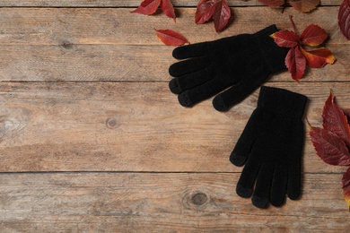 Stylish black woolen gloves and dry leaves on wooden table, flat lay. Space for text
