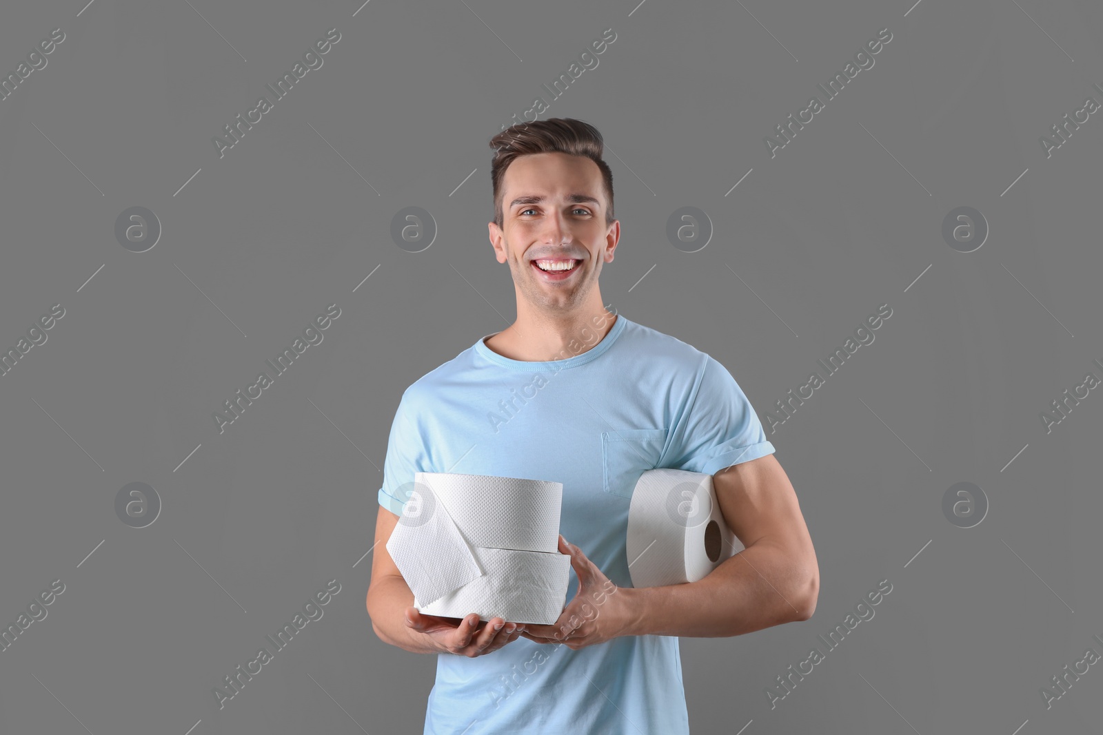 Photo of Young man holding toilet paper rolls on color background