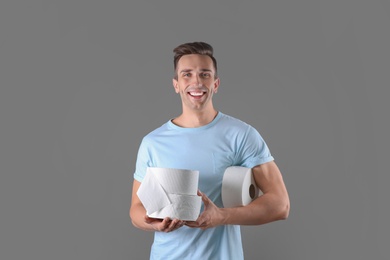 Young man holding toilet paper rolls on color background