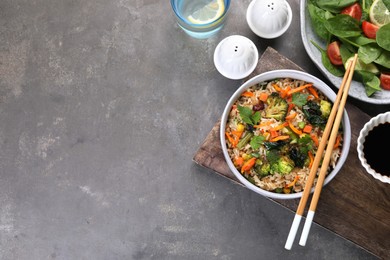 Tasty fried rice with vegetables served on grey table, flat lay. Space for text