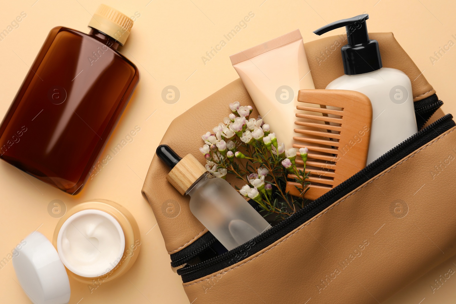 Photo of Preparation for spa. Compact toiletry bag with different cosmetic products and flowers on beige background, flat lay